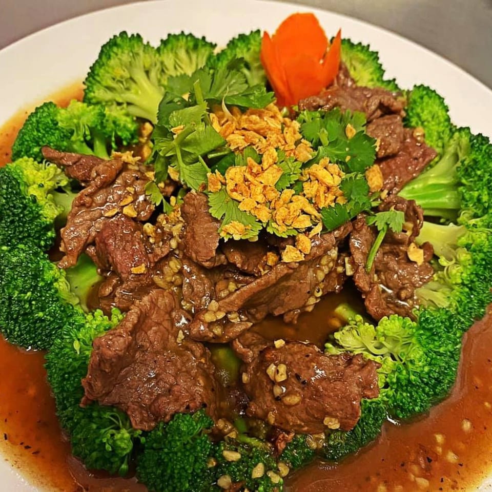 Thai E-San's beef and broccoli dish, garnished with cilantro, crispy garlic, and a carrot flower.