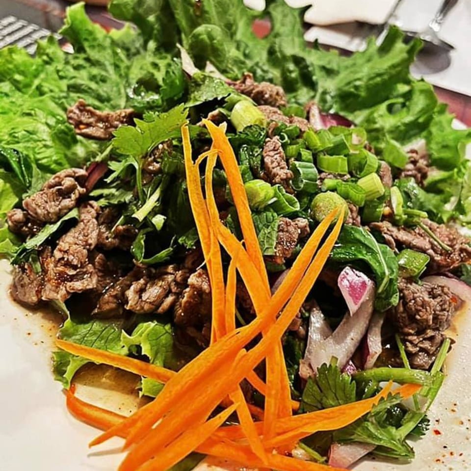 Thai E-San's beef salad with lettuce, green onions, cilantro, and shredded carrots on a white plate.