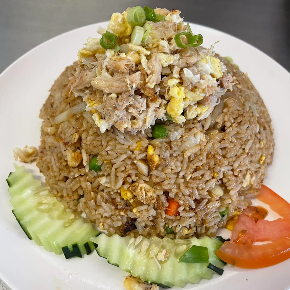 Thai E-San's crab fried rice, topped with scrambled egg, crab meat, and green onions, garnished with cucumber and tomato.