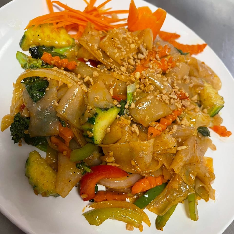 Close-up of Thai E-San's Pad See Ew with wide noodles, mixed vegetables, and crushed peanuts.