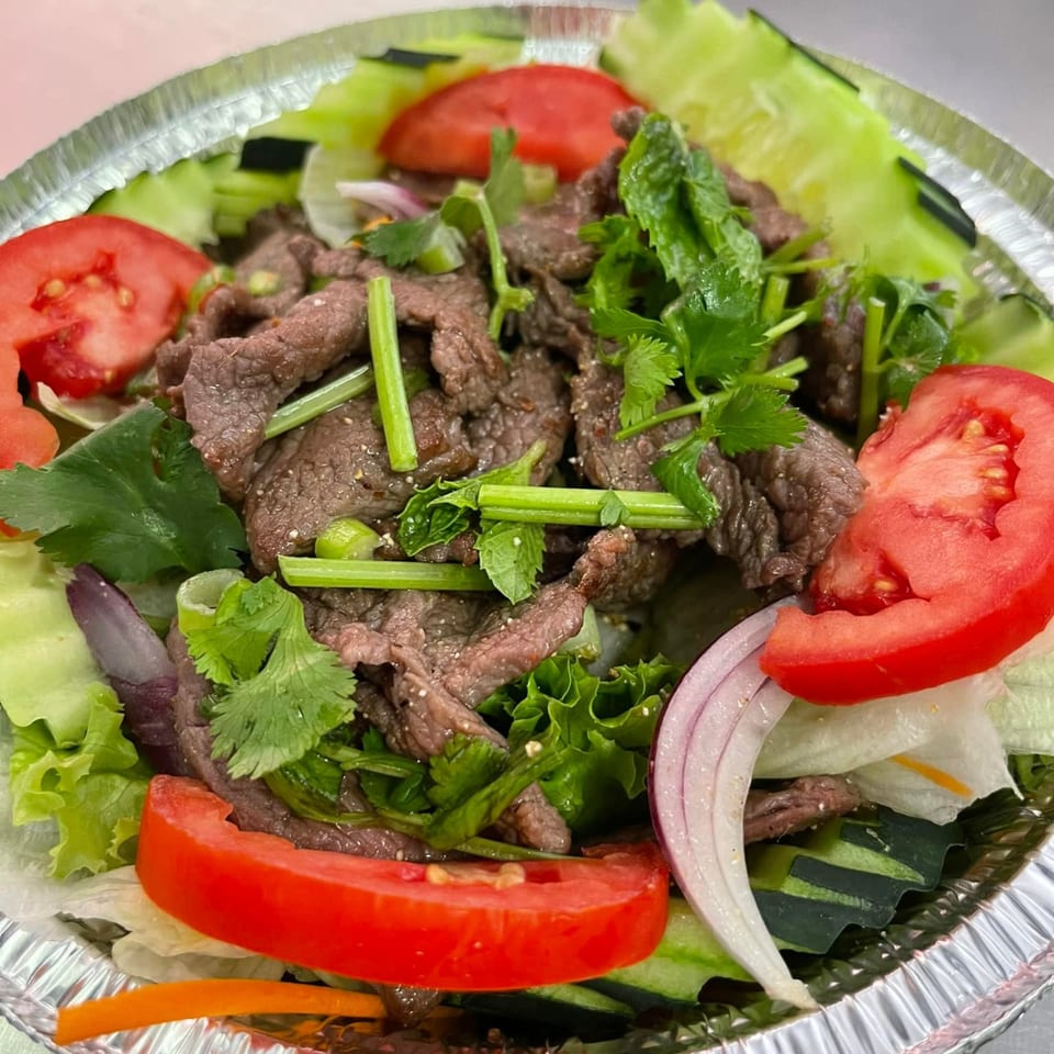 Thai E-San's Thai beef salad with tomatoes, cucumbers, red onions, and cilantro in a foil container.