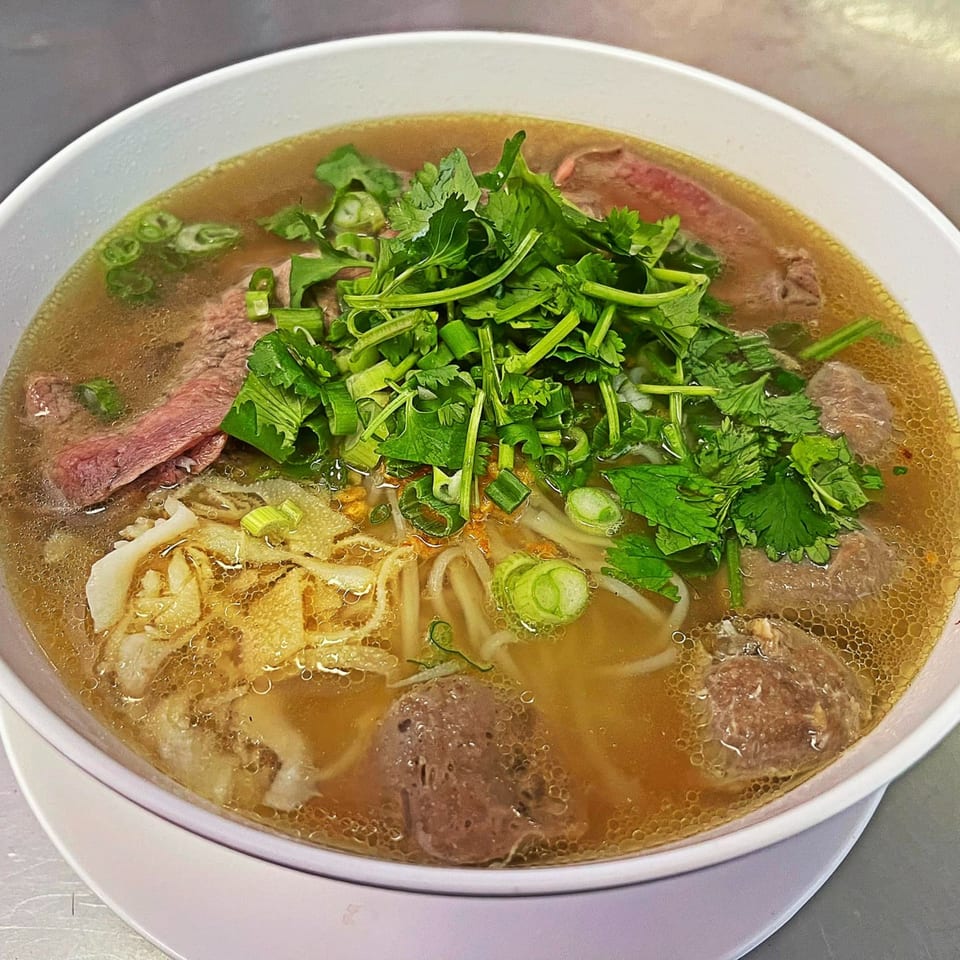 A bowl of Thai E-San beef noodle soup with cilantro, green onions, and beef slices.